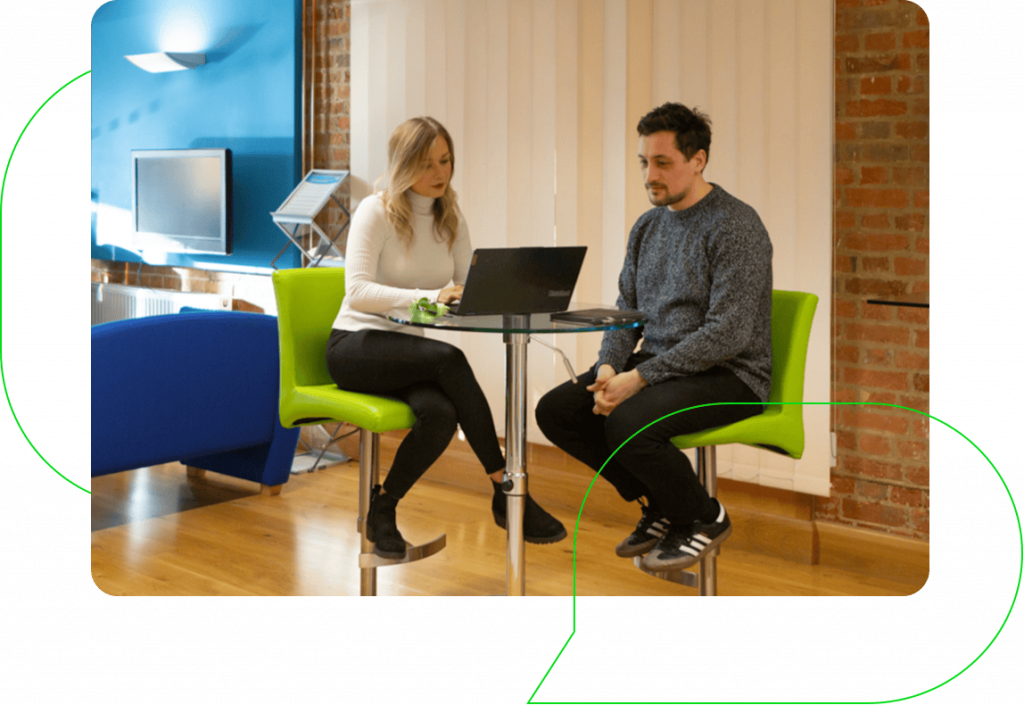 A woman and man sitting around a laptop in a modern office setting